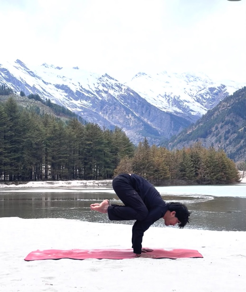 Bakasana crow pose practiced on a red mat by the lake with snow mountains