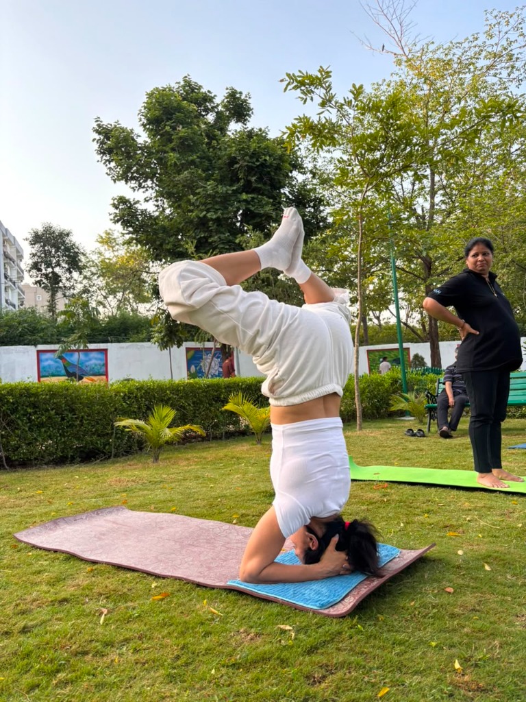 Practitioner doing a headstand variation pose (Sirsasana) on a mat in a park